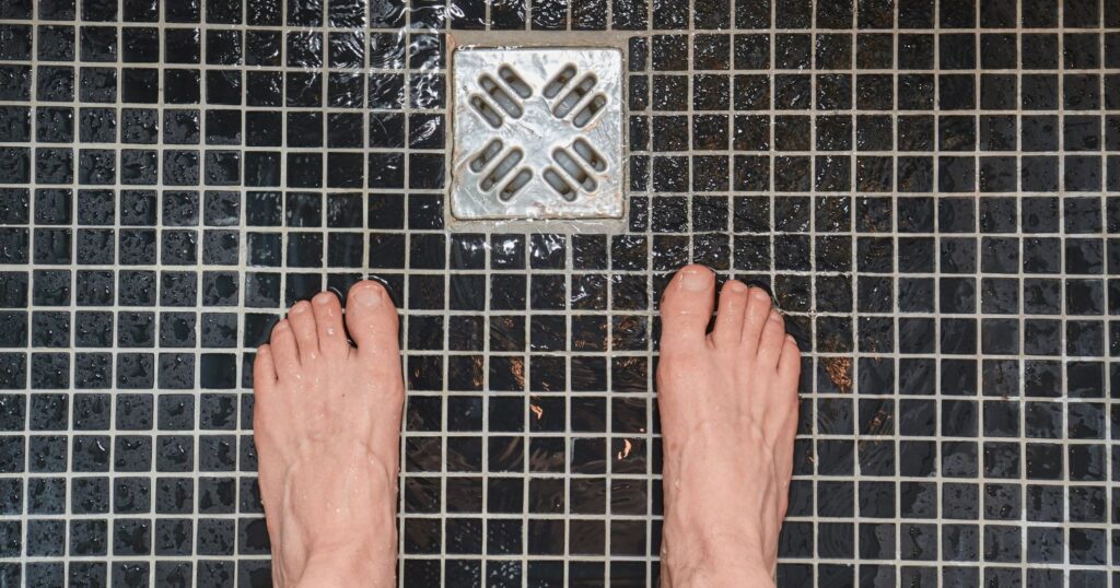 A képen egy láb látható a zuhanyban, a lábak előtt lefolyó