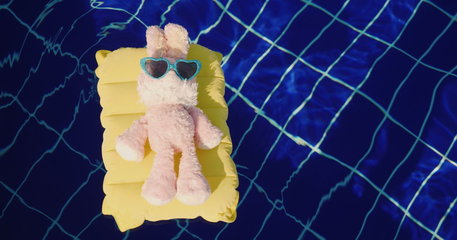 A képen egy medencében egy kicsi gumimatracon egy plüssállat napozik
