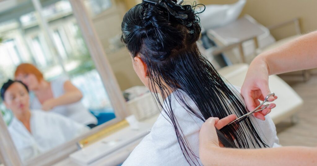 A képen egy fodrászatban egy nő ül a fodrász előtt, a haját vágják