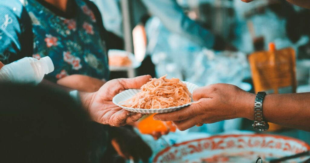 A kép egy ételosztáson készült, amint épp egy tányér ételt nyújtanak egy rászorulónak