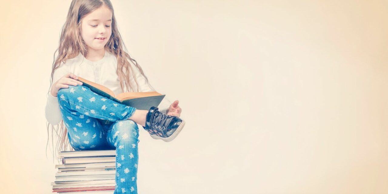 A képen egy kislány ül egy kupac könyvön, és olvas
