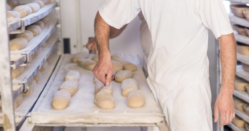 Pék munkaközben egy péküzemben, kenyeret süt.