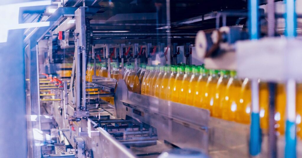 élelmiszeripari gyártósor van a képen, benne üdítősüvegek láthatók