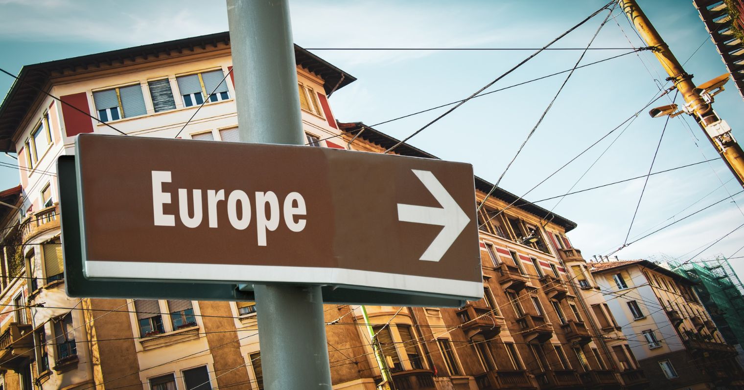 A képen egy utcarészlet látható, a kép középpontjában egy tábla látható, rajta az Európa felirat angolul, és egy nyíl