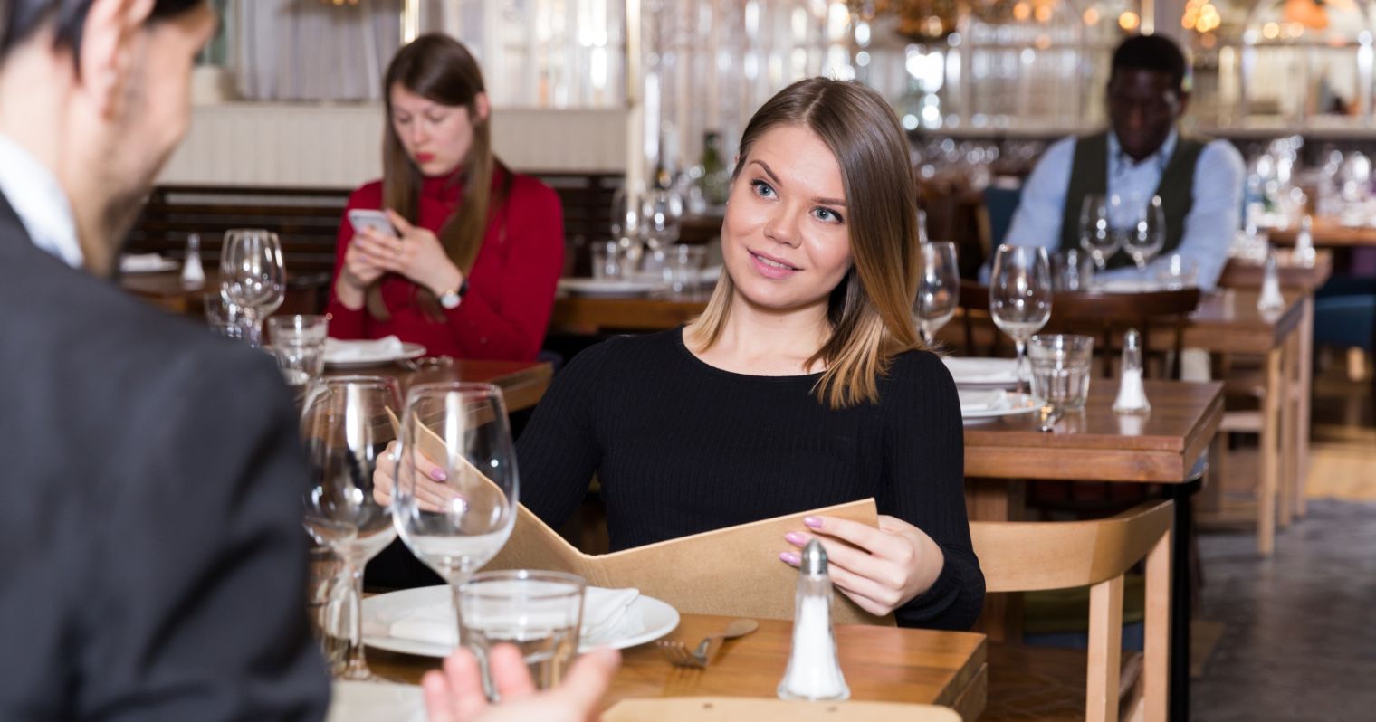 Egy fiatal nő néz egy étteremben egy fiatal férfira a menü felett