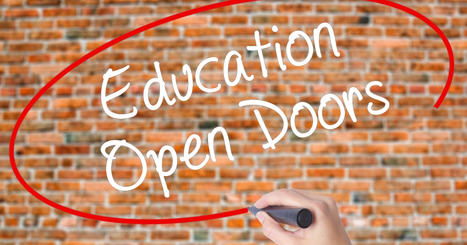 A képen egy téglafal látható, egy kéz az education open door feliratot karikázza be előtte