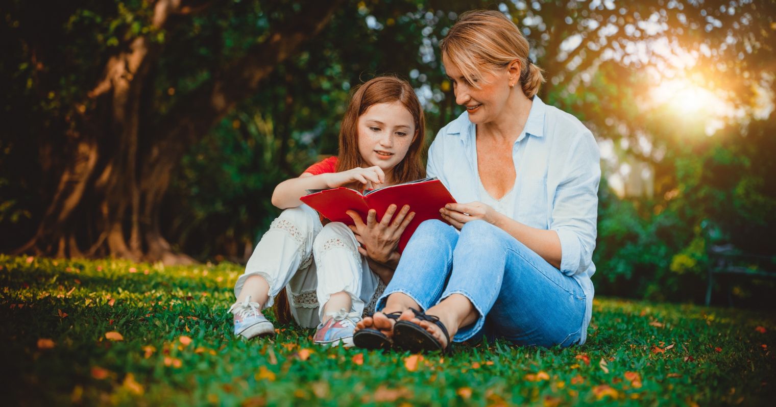 A képen egy parkban anyuka és lánya egy könyvből olvasnak