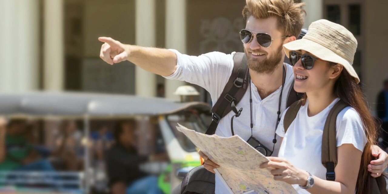 A képen egy férfi és egy női turista látható, kalapban, napszemüvegben, térképpel.