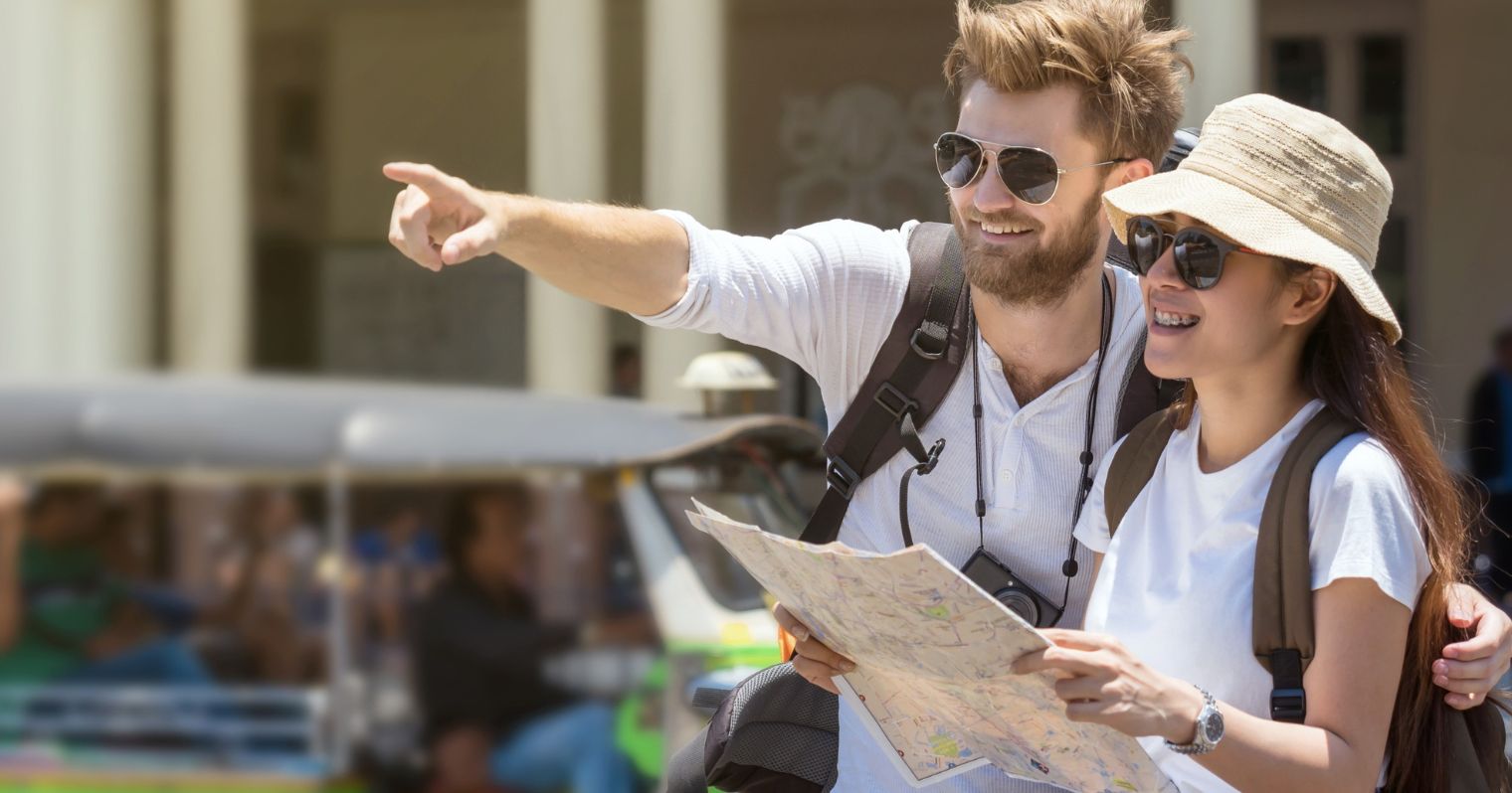 A képen egy férfi és egy női turista látható, kalapban, napszemüvegben, térképpel.