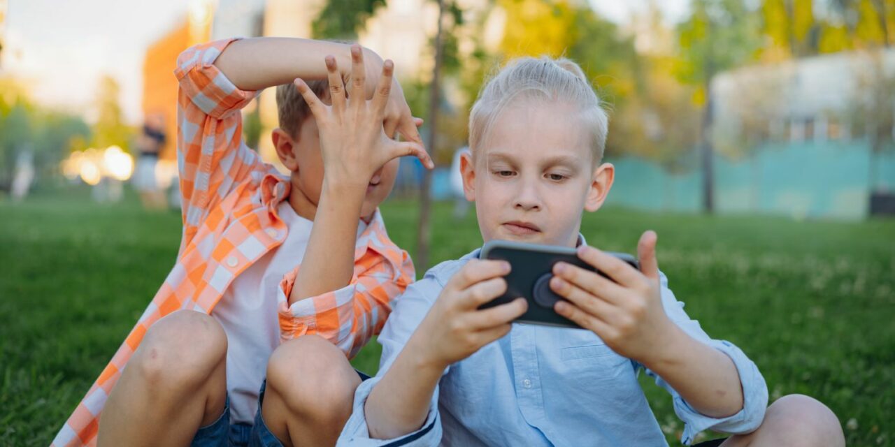 A képen telefonnal szórakozó gyerekek láthatók.