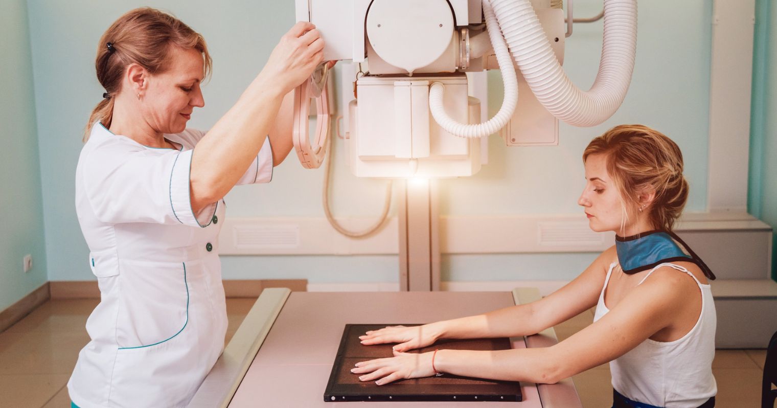 A képen egy radiográfiai szakasszisztens és a páciens látható, röntgen felvétel előkészítése közben.