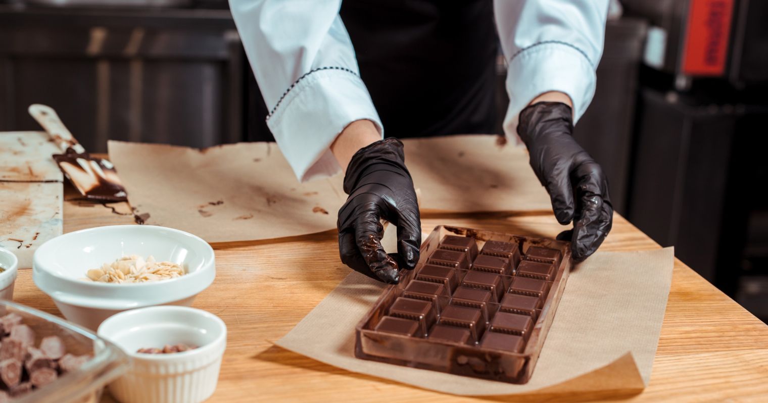 A képen a csokoládékockákat formázó édességkészítő keze látható.