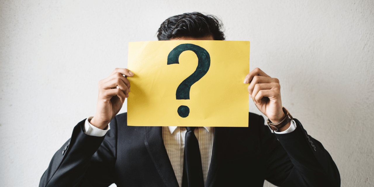 Fiatal öltönyös férfi az arca elé tartott papírlappal, ami egy nagy fekete kérdőívet ábr zol.