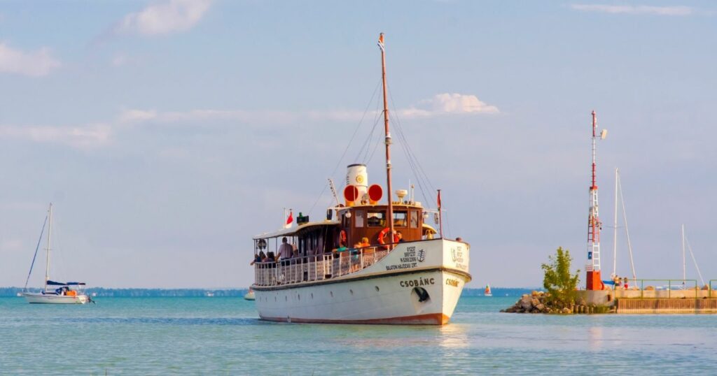 BAHART Csobánc nevű nosztalgiahajója épp befut egy kikötőbe a Balatonon.