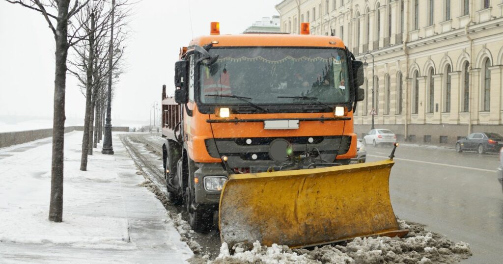 Hókotrógép előtte egy kupac hóval az út szélén áll.