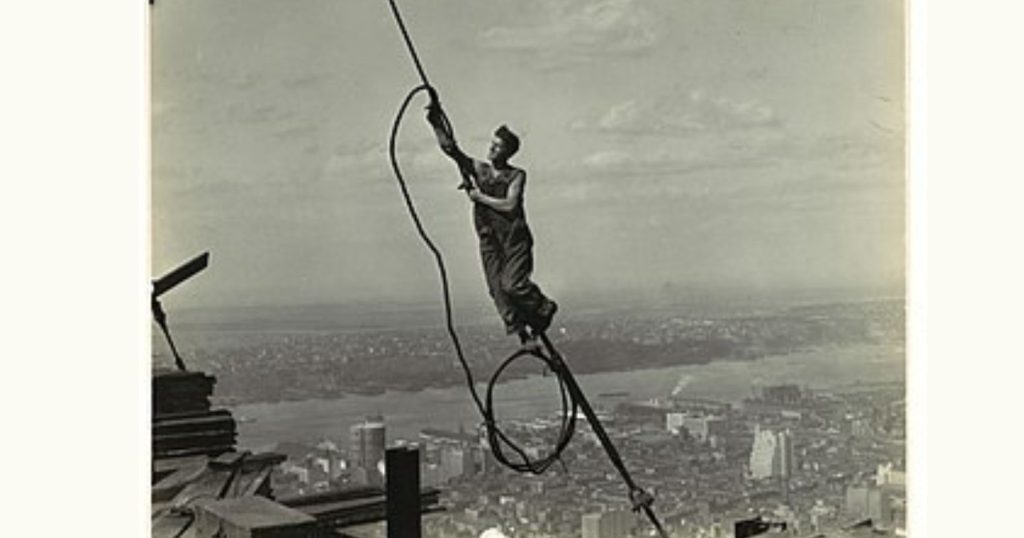 Empire State Building-et építő magasépítő mászik egy drótkötélen magasan, távol a talajtól.