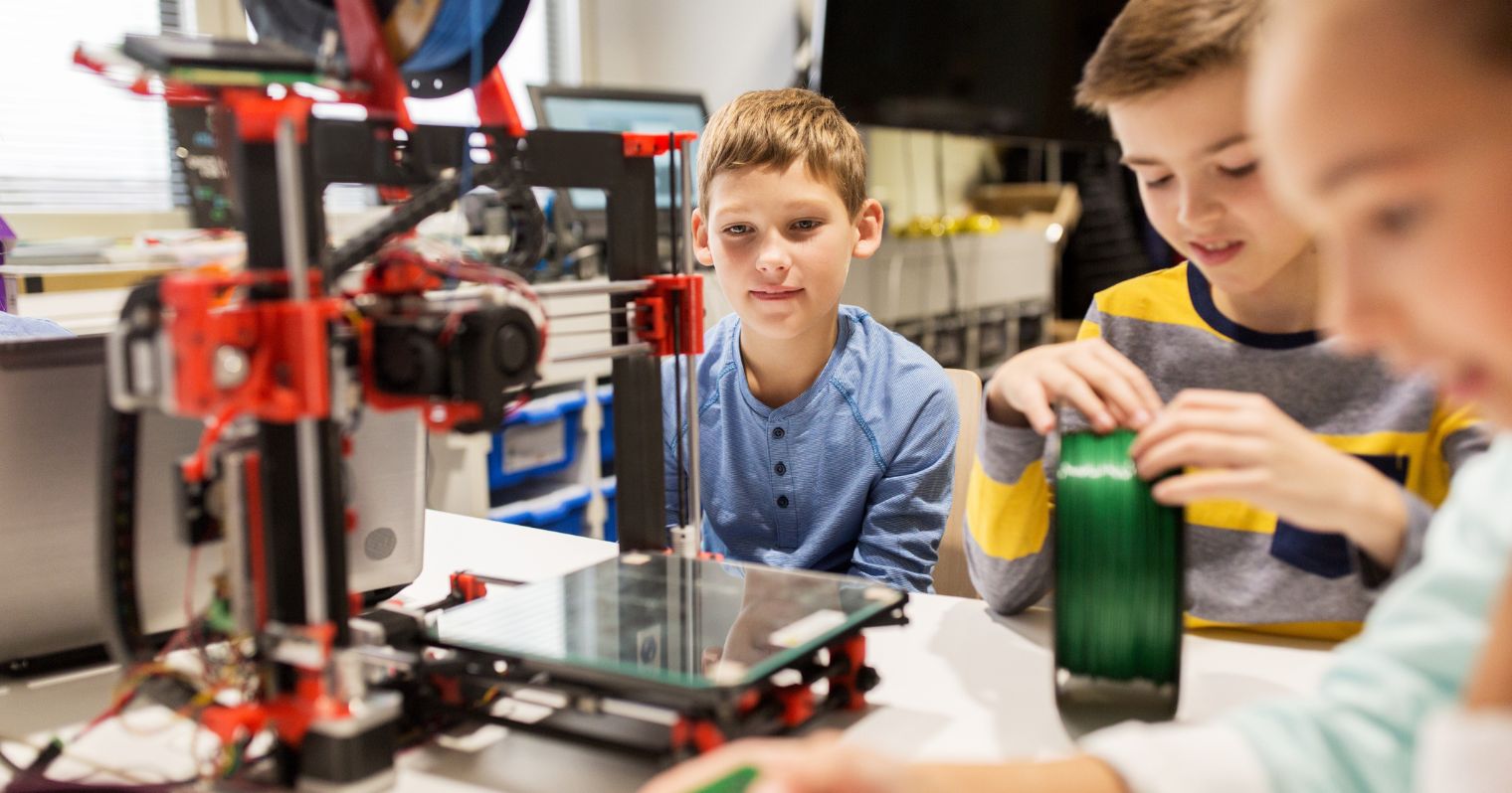 Iskolás fiúk ülnek körbe egy 3D nyomtatót.